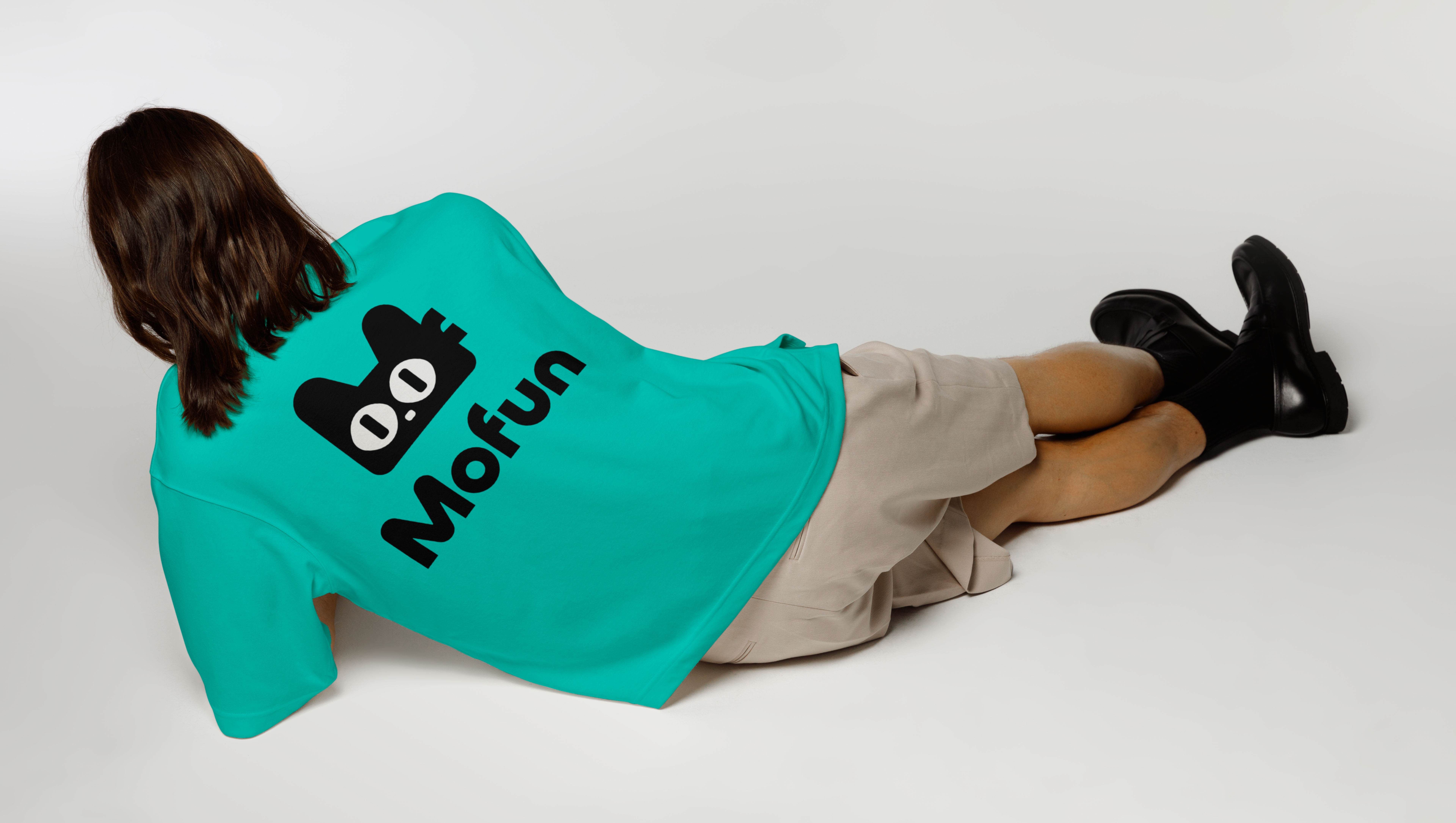 민트색 모펀 로고 티셔츠를 입고 바닥에 누워 있는 모델의 뒷모습
